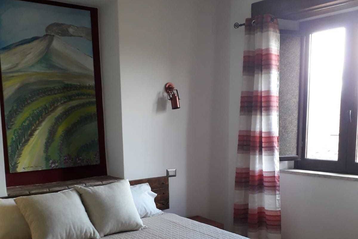 A bedroom with a bed, pillows, a painting, a nightstand, a lamp, and a window with curtains.