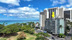 A high-rise hotel with multiple balconies, a view of the ocean, and a parking area.