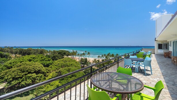 A balcony with a view of the ocean and beach, green chairs, and a table.