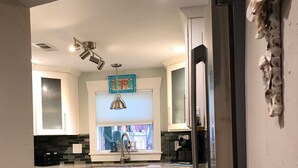 A kitchen with white cabinets, a stainless steel refrigerator, a window with blinds, and a hanging pendant light.