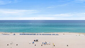 A wide beach with a clear sky, a few umbrellas, and a small structure in the middle. - Spectacular Ocean Villa END Unit 1001 - Coastal Decor and Endless Views! (Panama City Beach)