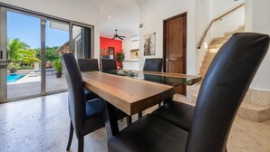 A modern dining area with a glass-top table and black chairs, a wooden door, and a staircase.