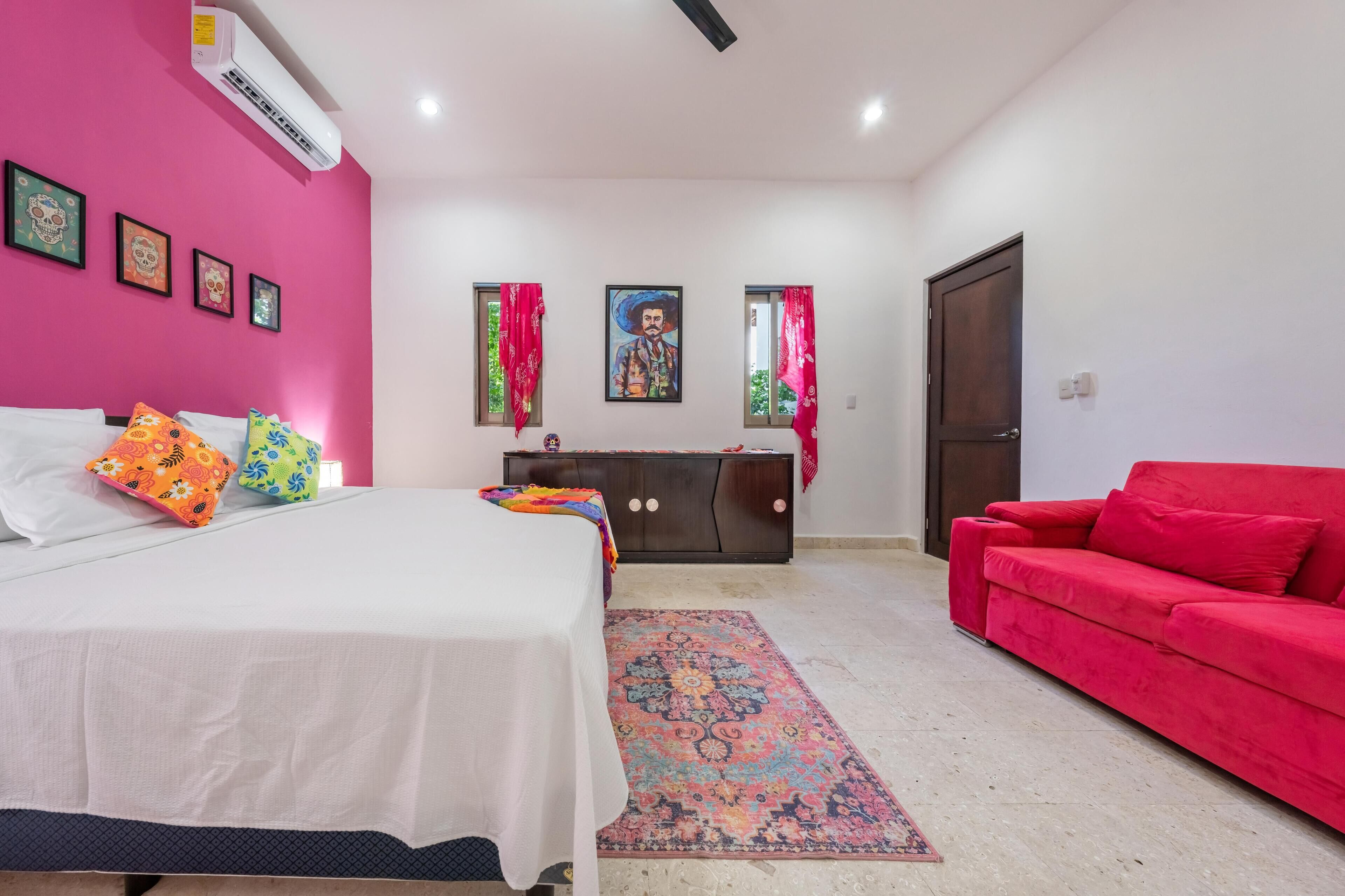 Une chambre à coucher avec un lit, un canapé rouge, une commode et un tableau accroché au mur.