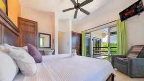 A hotel room with a large bed, a TV mounted on the wall, a balcony with a view, and a wooden door.