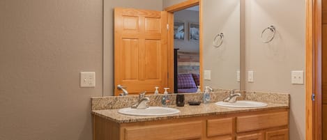 Un baño con tocador doble, dos lavamanos, un espejo grande y una puerta de madera.