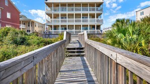 A wooden boardwalk leading to a multi-story building with balconies, surrounded by greenery. - Mid beach ocean front 3 bedroom 2 bath condo (Tybee Island)