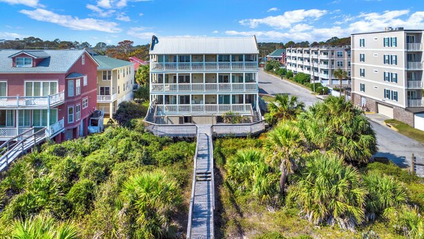 A multi-story building with balconies, surrounded by lush greenery and a wooden walkway leading to the entrance. - Mid beach ocean front 3 bedroom 2 bath condo (Tybee Island)