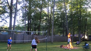 A backyard with a volleyball net, a fire pit, and a wooden fence. - Walk to Lake cottage with beautiful Higgins Lk "Gold Coast" access (Roscommon)