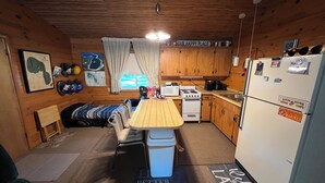 A compact cabin-style kitchen with wooden cabinets, a stove, a refrigerator, and a small dining table. - Walk to Lake cottage with beautiful Higgins Lk "Gold Coast" access (Roscommon)