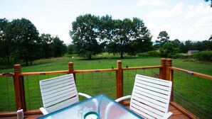 Een terras met twee witte stoelen en een glazen tafel, met uitzicht op een gazon met bomen en een gebouw in de verte.