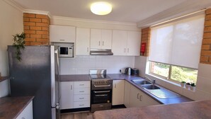 Una cocina compacta con armarios blancos, un refrigerador de acero inoxidable, un microondas, una estufa y un lavaplatos.