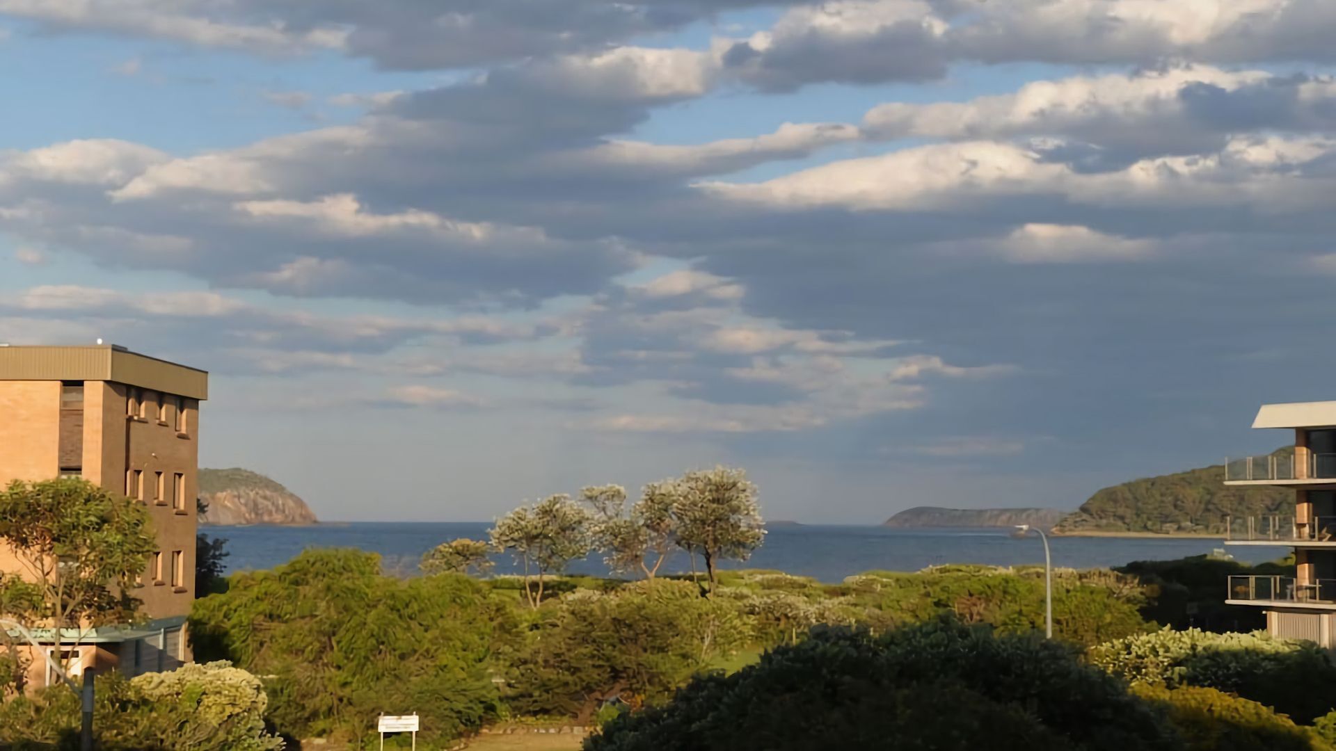 A coastal view with buildings, trees, and a clear sky.