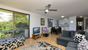 A modern living room with a large window, a ceiling fan, a dining area, and a kitchen.