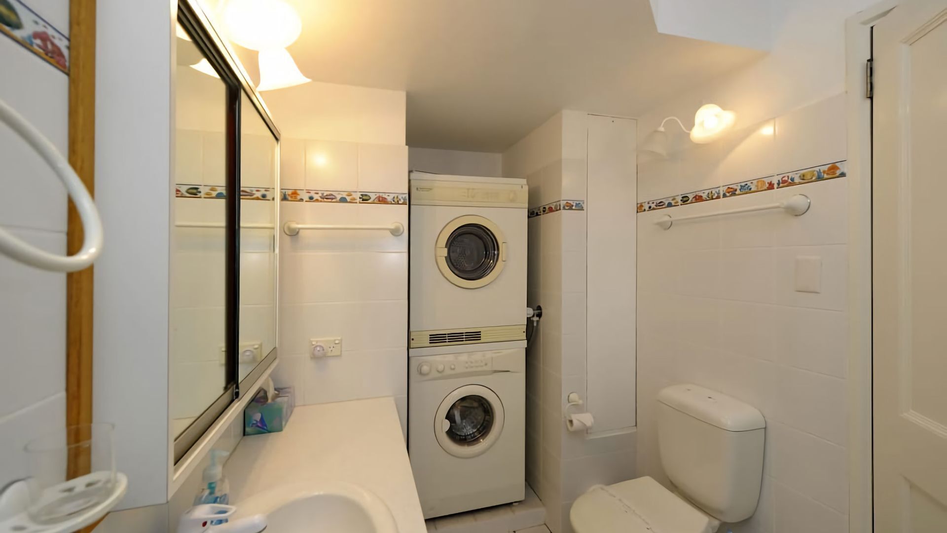A compact bathroom with a toilet, a sink, and a double washing machine.
