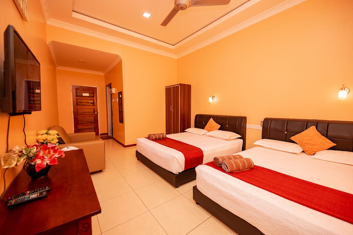 A hotel room with two beds, a desk with a vase of flowers, a television, and a ceiling fan.