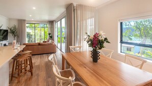A modern living room with a wooden dining table, white chairs, and a beige sofa. - Oasis 2, Beautiful Apartment on Hamilton Island (Whitsundays)