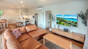 A modern living room with a leather sofa, wooden coffee table, and a large flat-screen TV displaying a scenic view. - Oasis 2, Beautiful Apartment on Hamilton Island (Whitsundays)