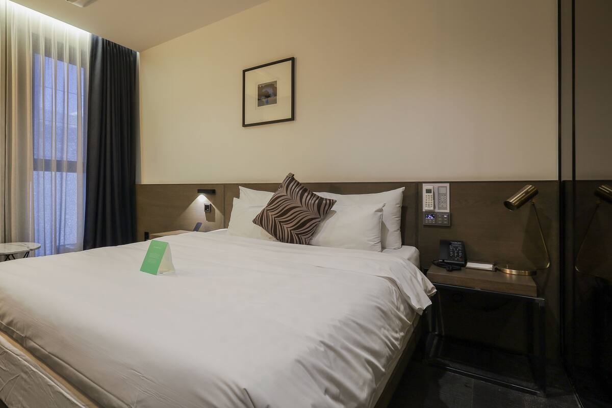 A hotel room with a large bed, a bedside table with a lamp, a phone, and a small table with a chair.