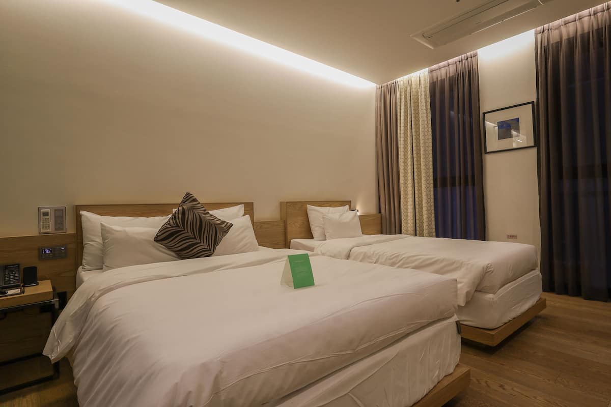 A hotel room with two beds, a bedside table with a lamp, a phone, and a green sign.