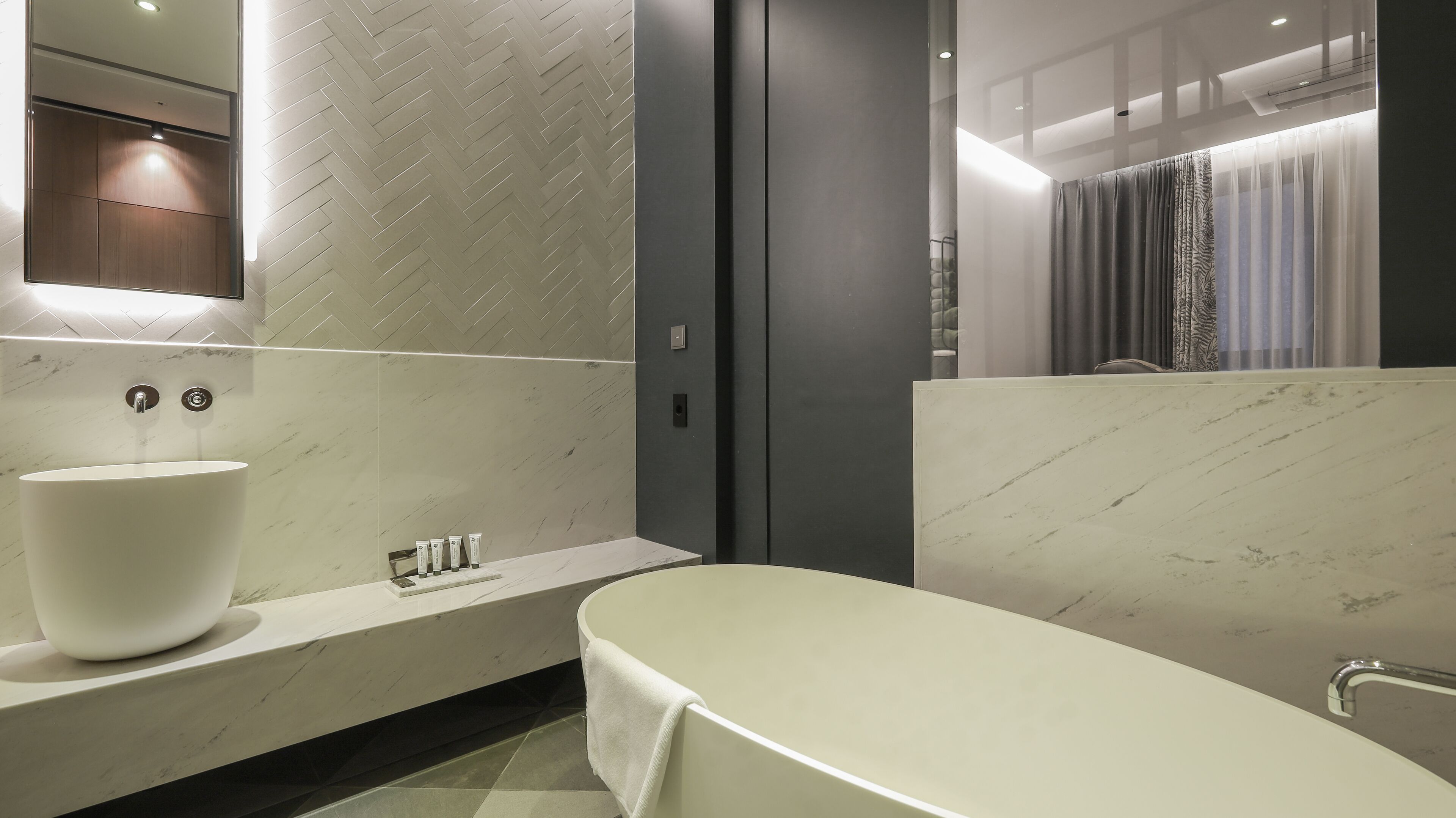 Un baño moderno con un lavamanos grande de color blanco, una bañera y un espejo sobre el lavamanos.