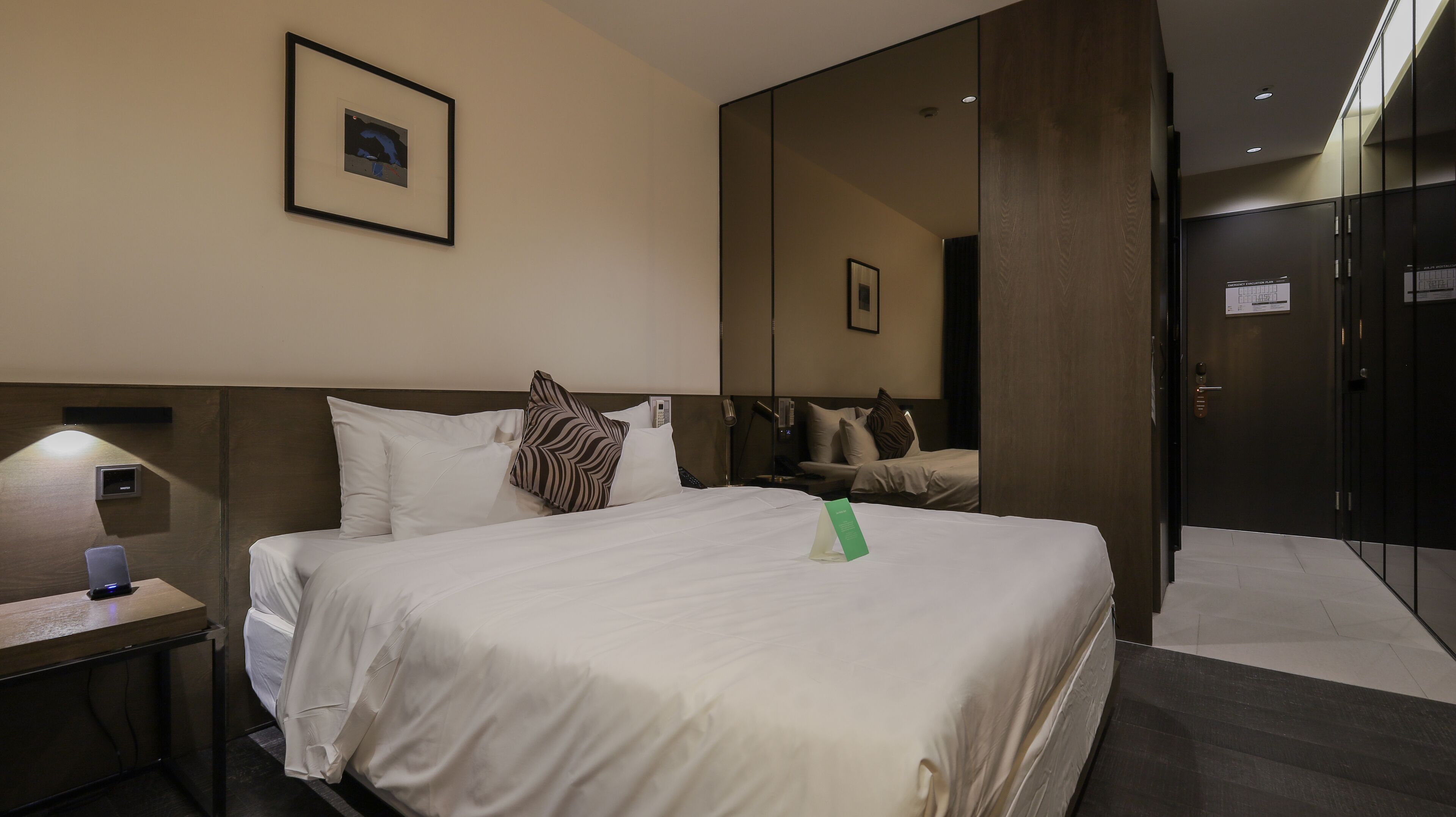 A hotel room with a large bed, a bedside table with a lamp, a mirror, and a framed picture on the wall.