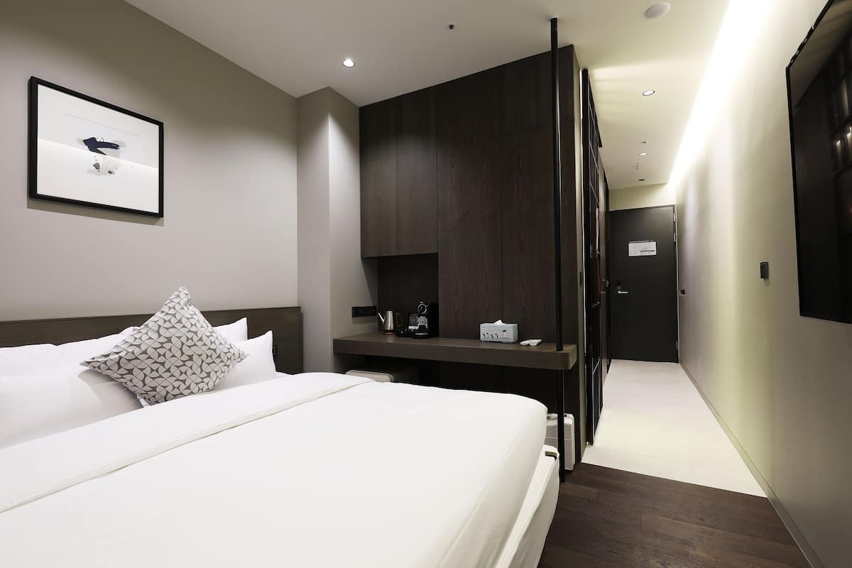A modern hotel room with a large bed, a desk with a coffee maker, and a framed picture on the wall.