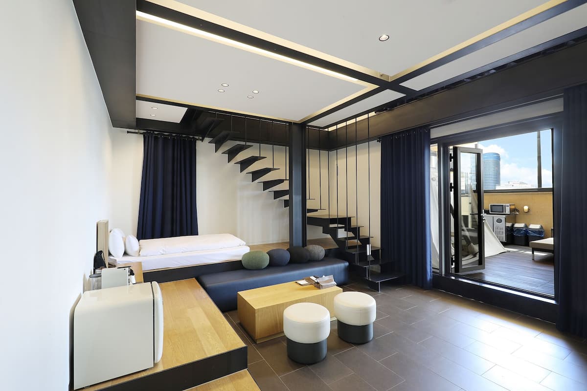 A modern hotel room with a bed, seating area, and a staircase.