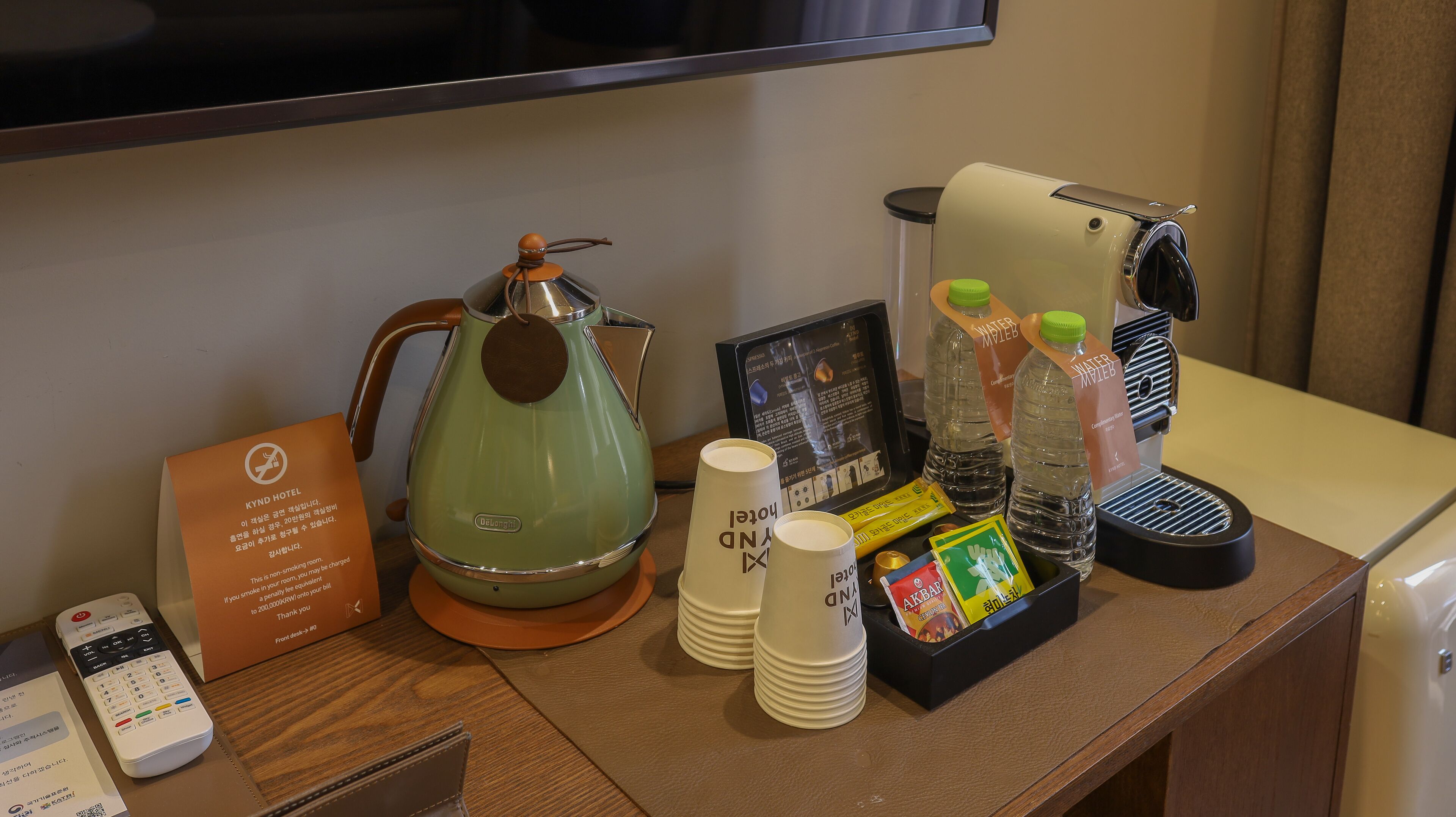 A hotel room with a coffee maker, a kettle, a water dispenser, and a remote control on the table.