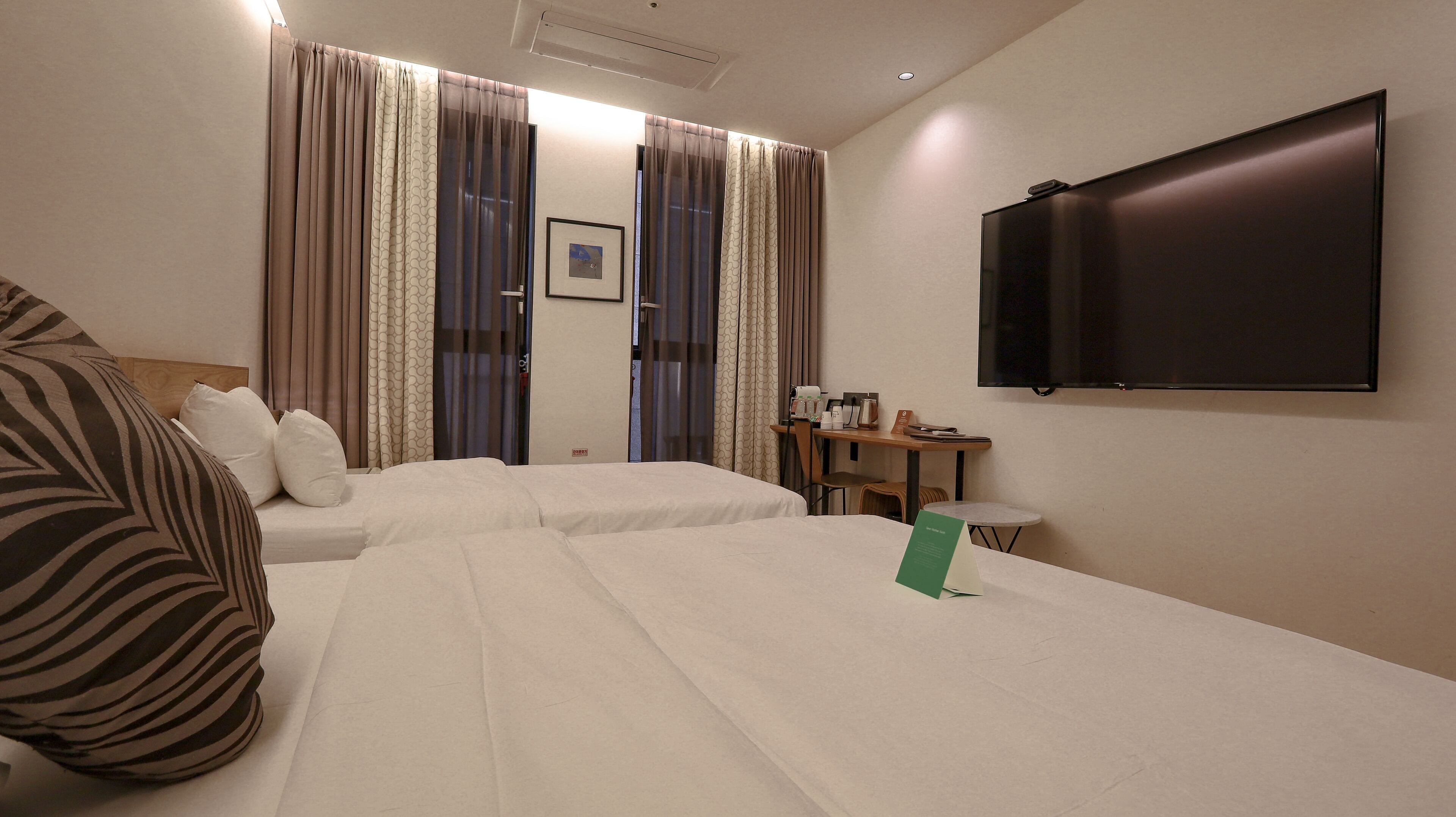 A hotel room with two beds, a desk, a chair, a television, and curtains.