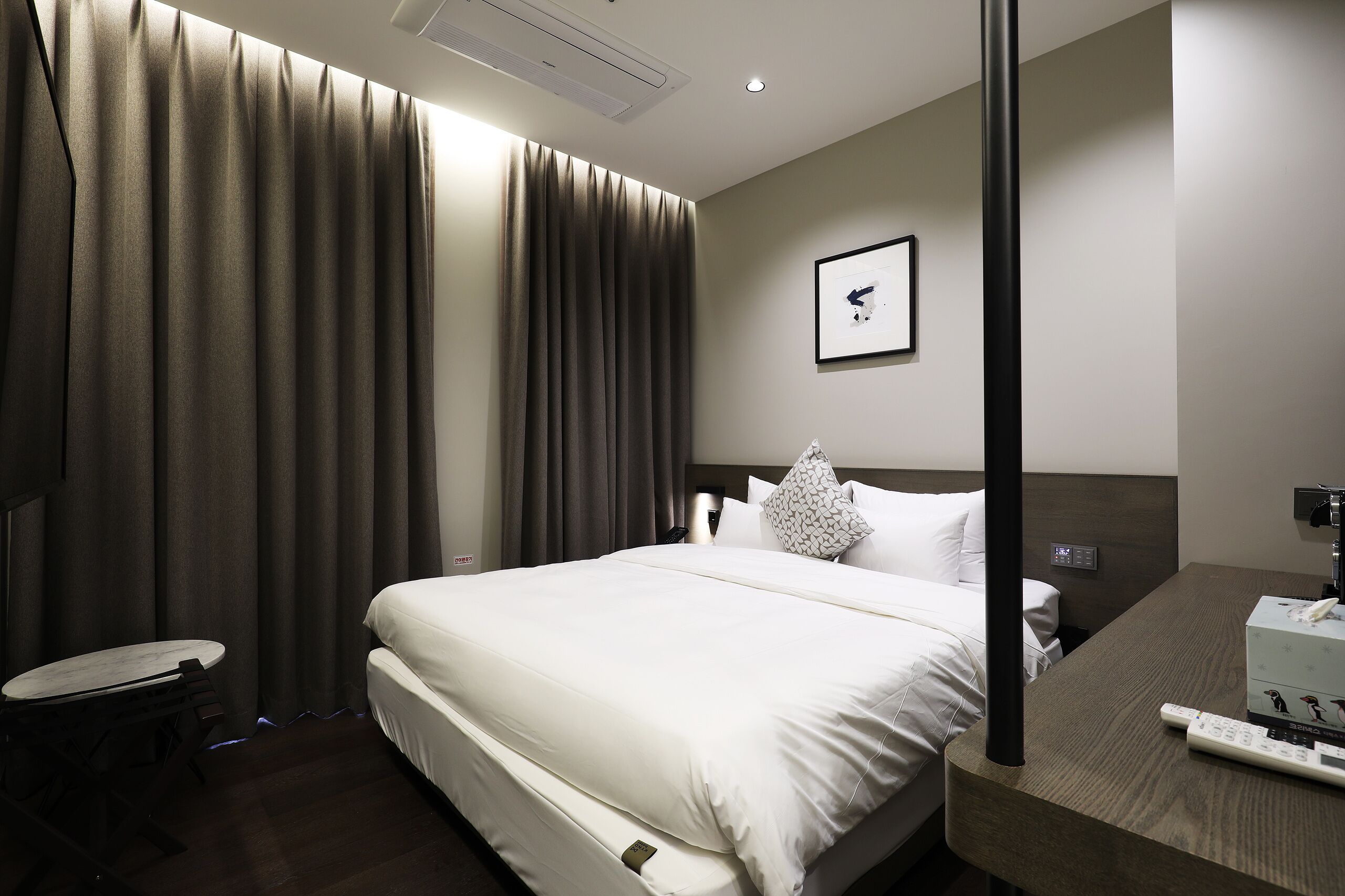 A hotel room with a bed, a bedside table, a chair, a desk, and a wall-mounted TV.