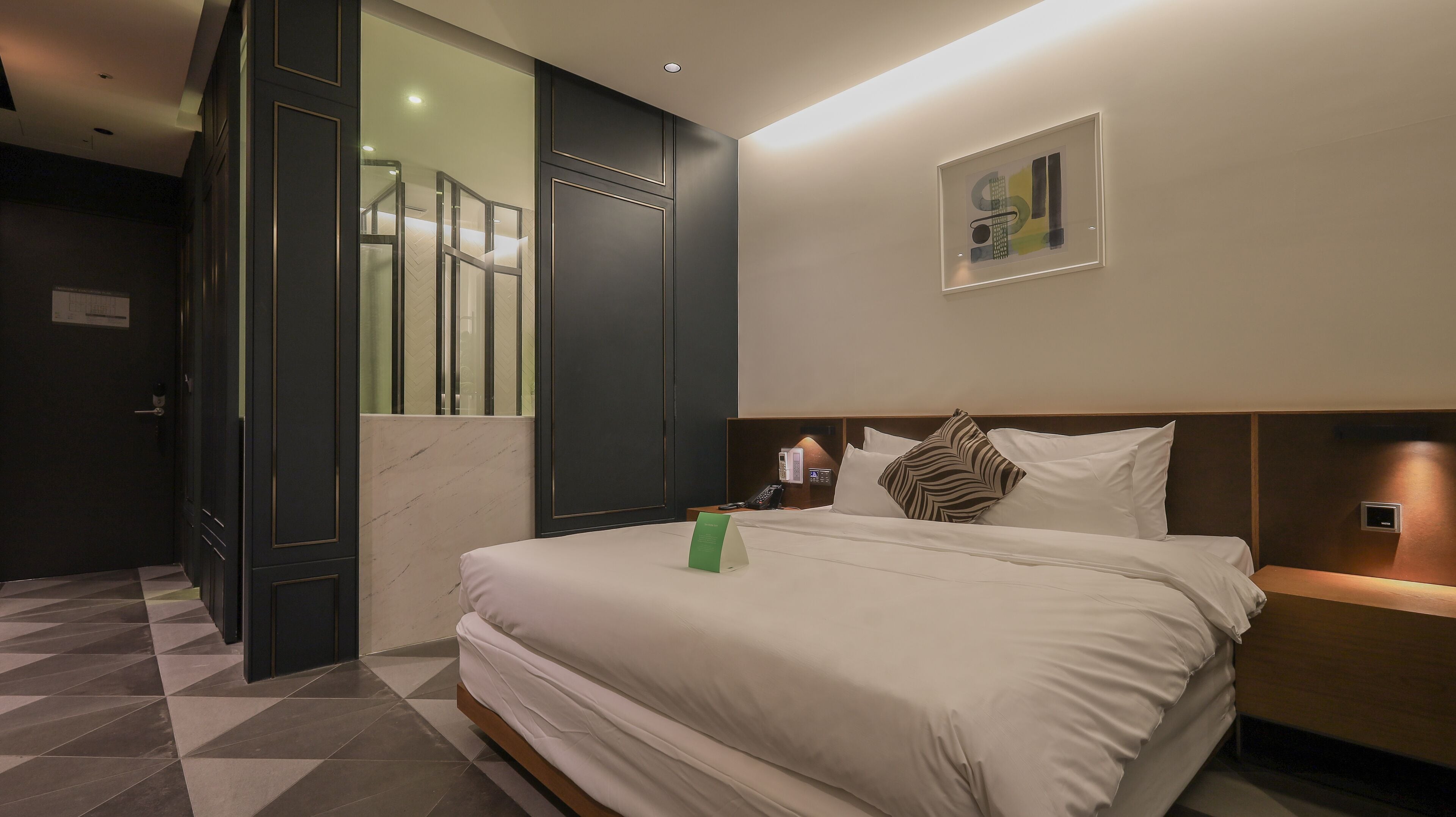 A hotel room with a bed, a bedside table, a wall-mounted phone, and a framed picture.