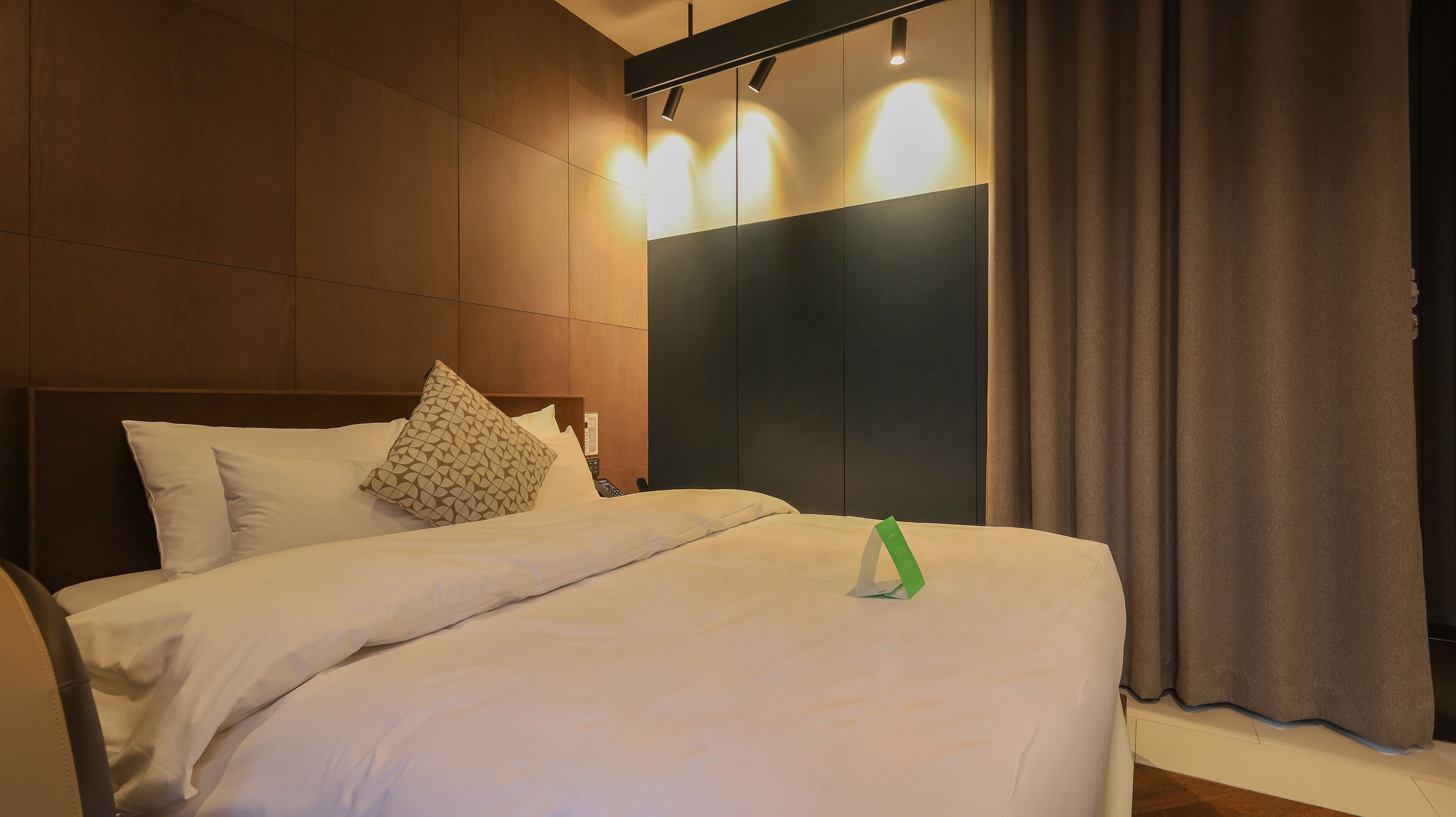 A hotel room with a large bed, a headboard, a bedside table, and a curtain.