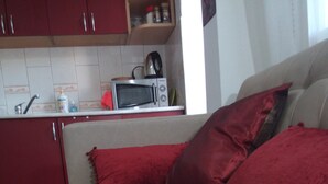 A bedroom with a bed, red pillows, and a kitchenette in the background. - TMC Skopje Apartment (Skopje)