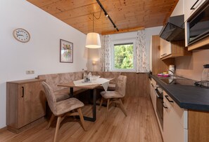 Cocina compacta con muebles de madera, una mesa de comedor con sillas, una ventana con cortinas y un reloj en la pared.