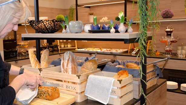 Zona de bufé con diversas opciones de comida, incluyendo pan y pasteles, expuestos en cajas de madera.