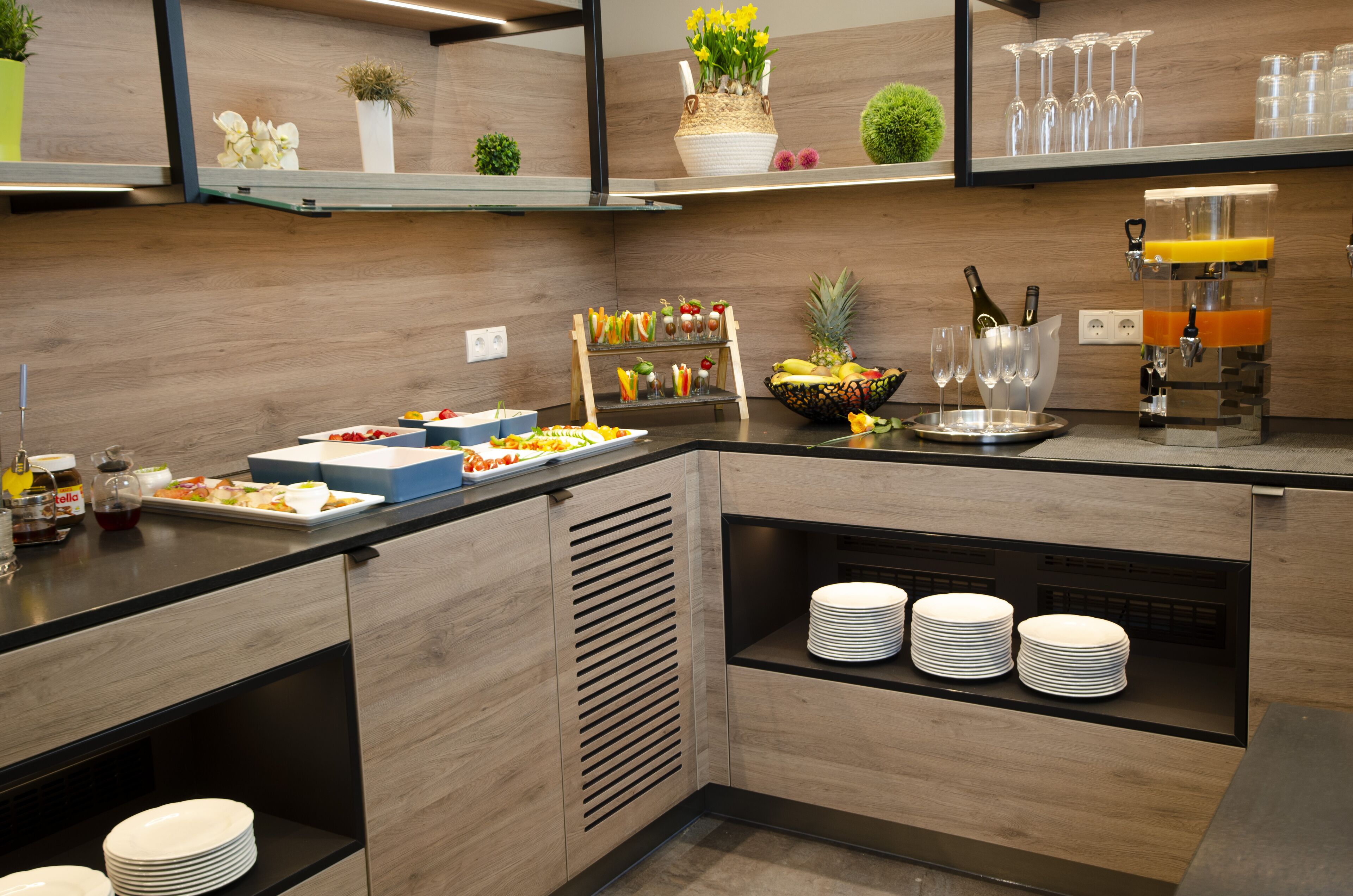 A modern kitchen with a buffet setup including a fruit bowl, drinks, and a variety of dishes.