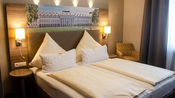 A hotel room with a large bed, two bedside tables, a chair, and a wall-mounted painting of a building.