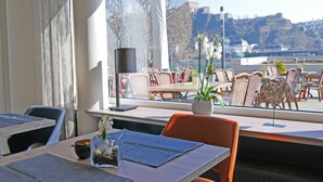 Un restaurante con terraza, vistas a un castillo y una mesa con un jarrón de flores.