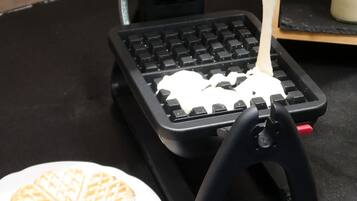 A waffle iron on a black countertop with a hand pouring batter onto it.