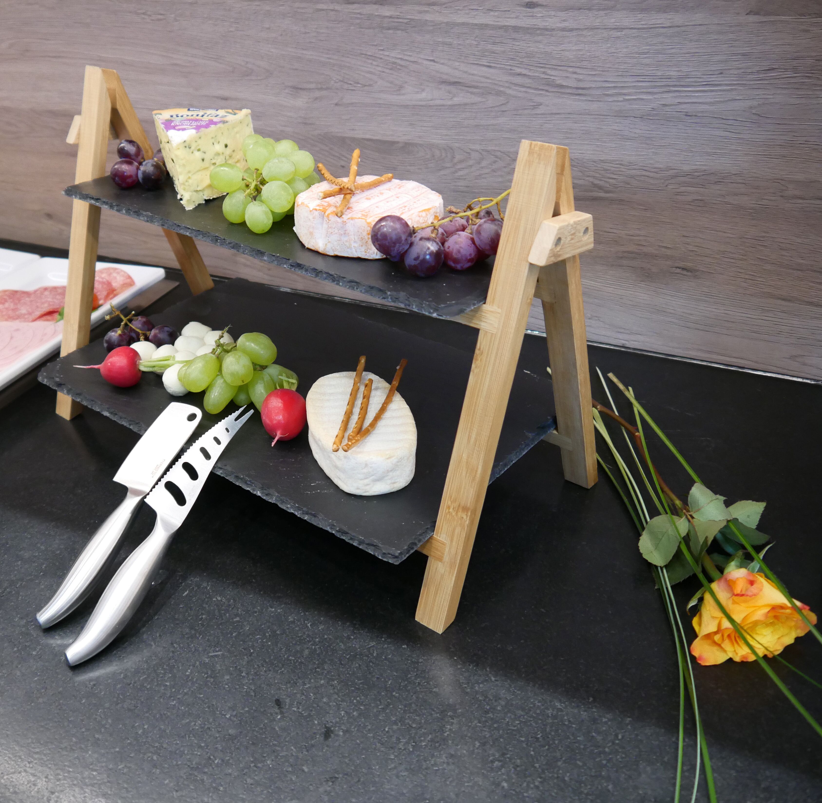 A cheese board with various cheeses, grapes, and crackers on a wooden stand.