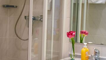 Un baño con cabina de ducha de vidrio, lavabo con espejo y una botella de champú.