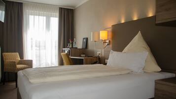 A hotel room with a large bed, a desk, a chair, and a lamp.
