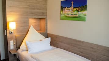 A hotel room with a bed, a nightstand with a lamp, a wooden headboard, and a painting of a cityscape on the wall.