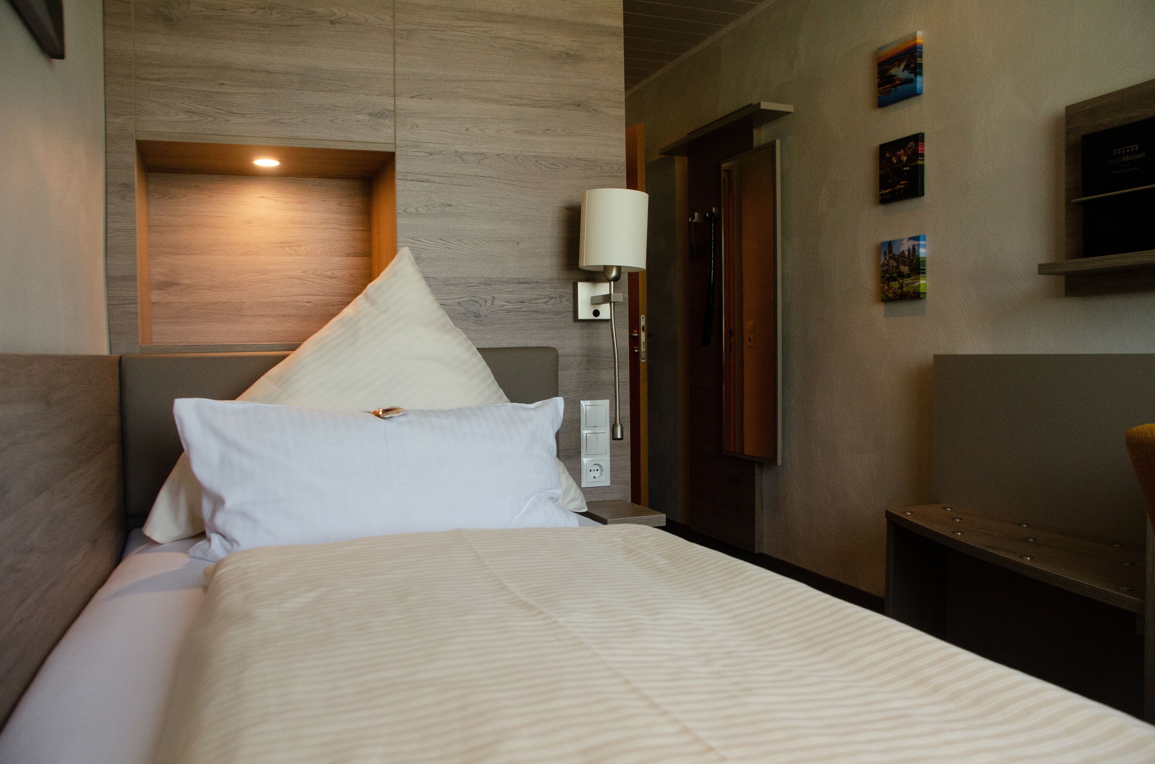 Ein Hotelzimmer mit Bett, Nachttisch, Wandlampe und Tür.