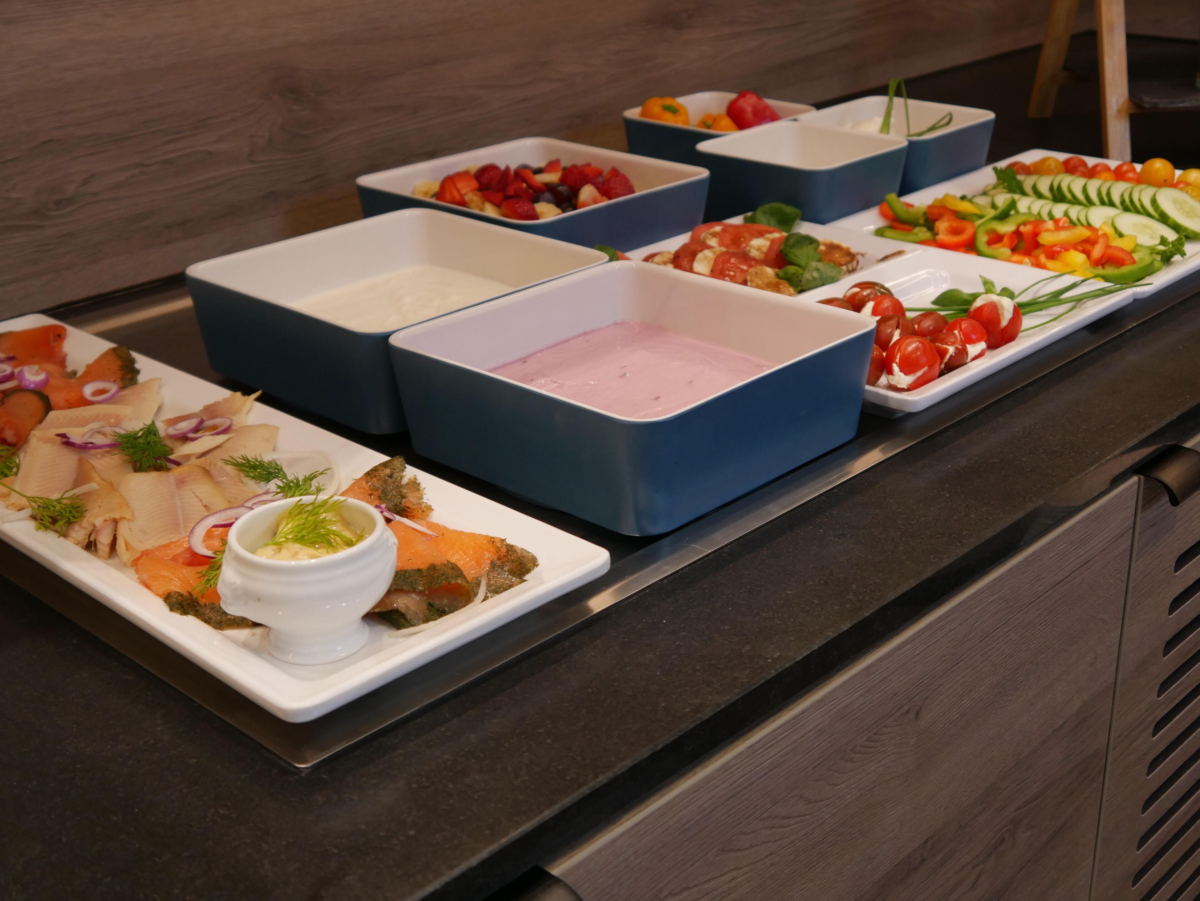 A buffet table with various food items including salmon, fruits, and vegetables.