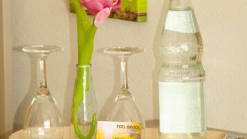 A tray with a glass vase containing a pink flower, a bottle of water, and a glass.