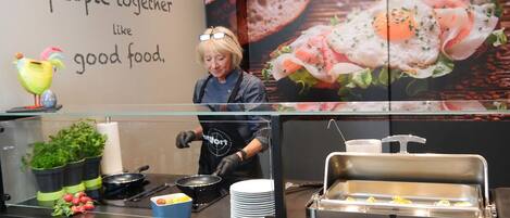 A buffet setup with a chef preparing food, a sign with a message, and various food items displayed.