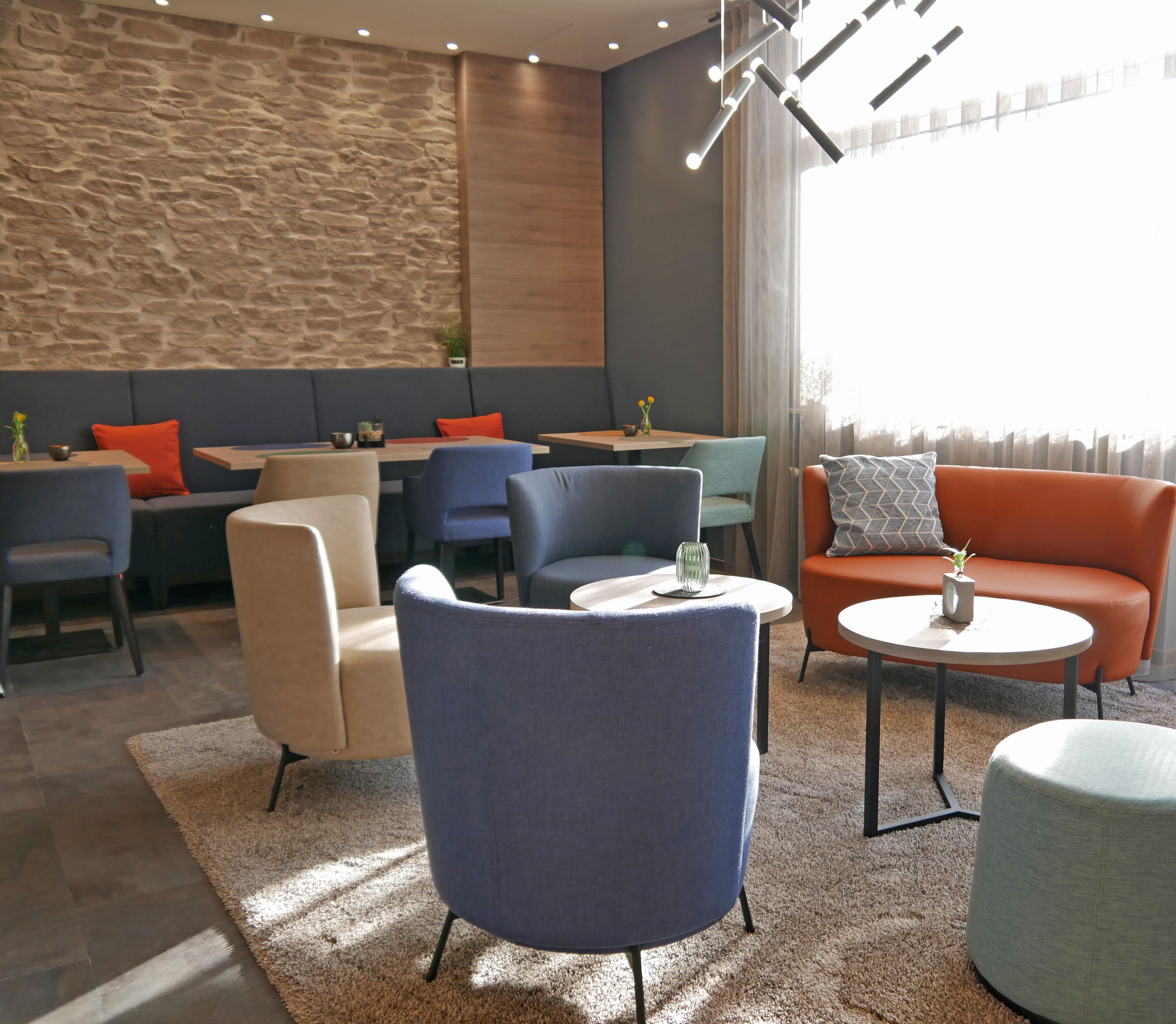 A modern lounge area with seating arrangements, a stone wall, and a large window.