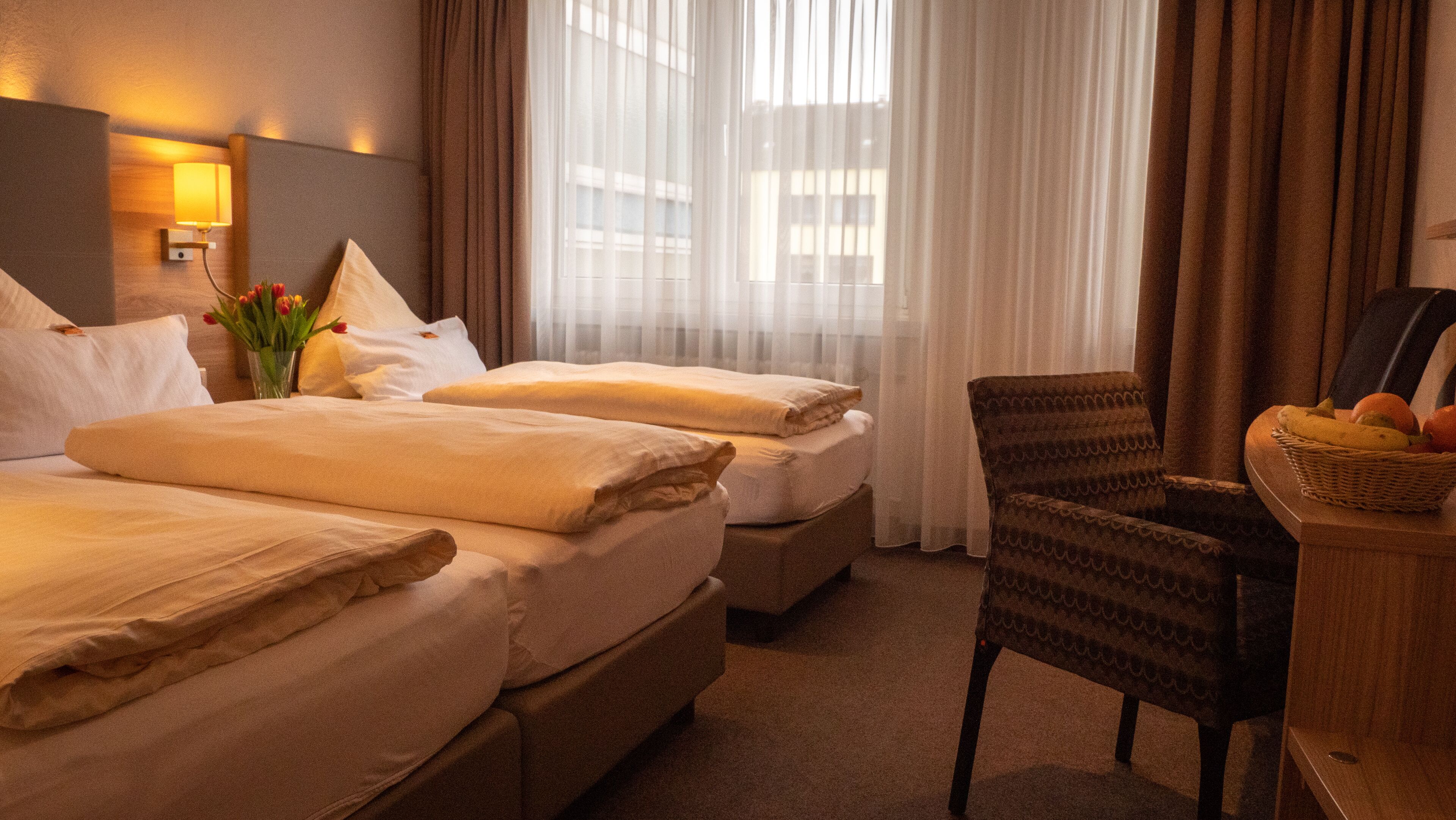 A hotel room with two beds, a chair, a desk, and a window with curtains.