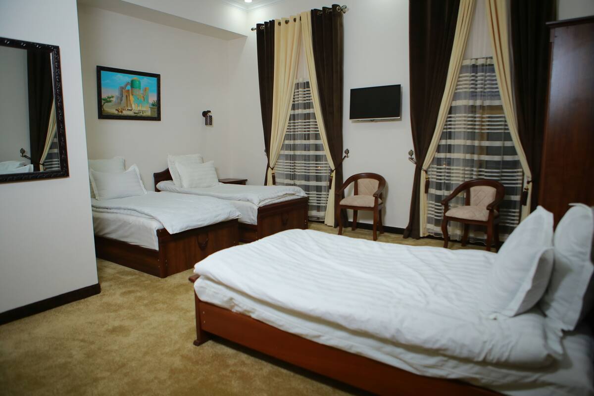A hotel room with two single beds, a wooden chair, a small table, a painting on the wall, and a television.